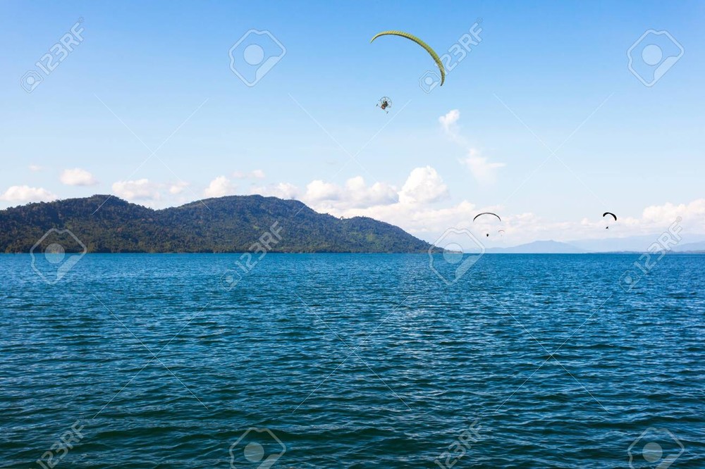 146187721-parachute-flying-over-water-surface-with-background-mountains-trees-and-mist-on-a-clear-day-in-laos-.jpg